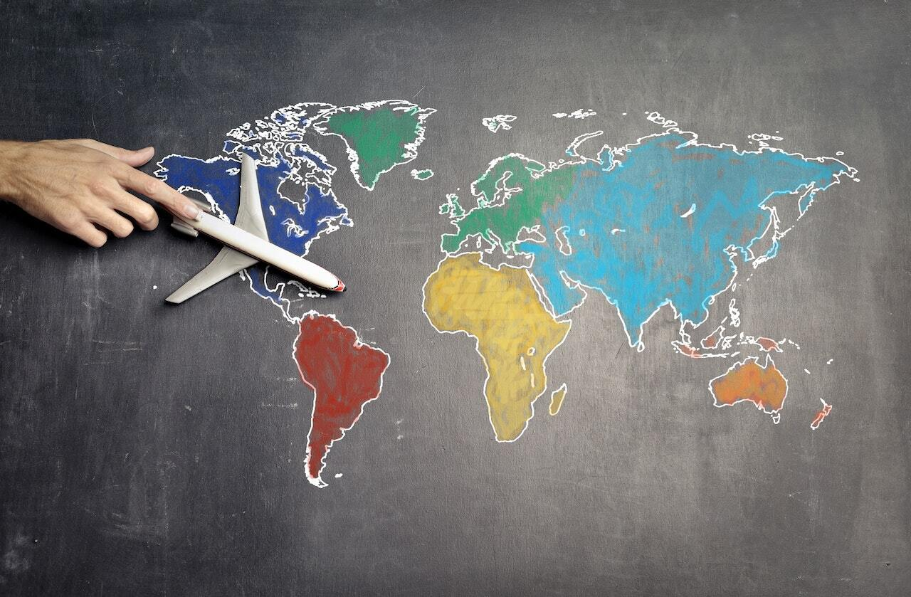 A hand moving a model plane across a chalk-drawn world map